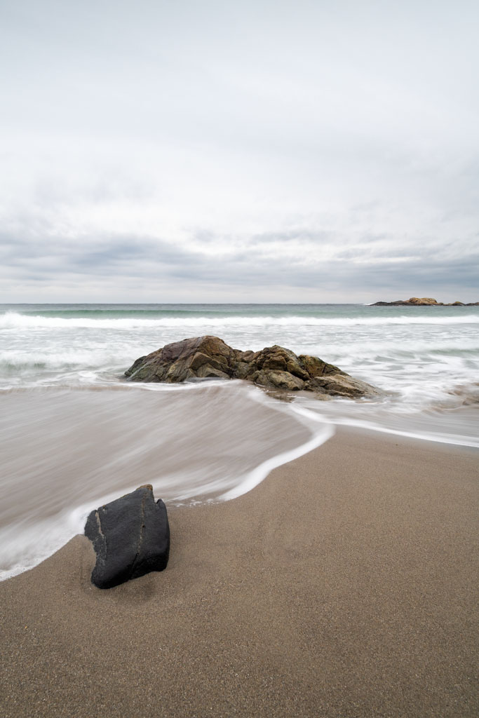 Bølger som ruller inn over sand og spredte steiner på Haviksanden.