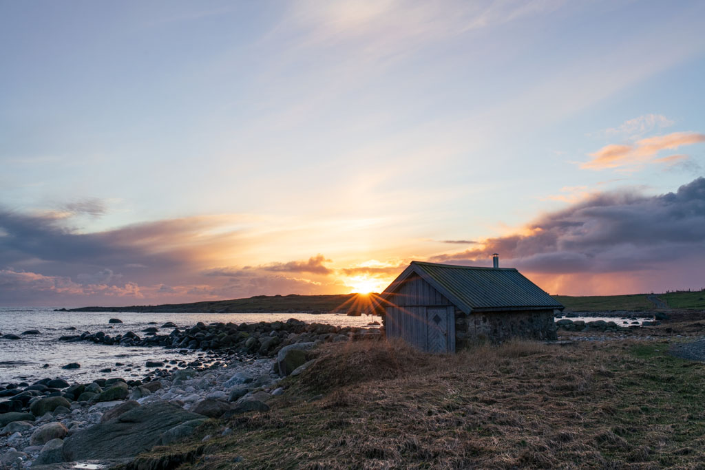 Naust ved Østhasselstrand badet i varmt solnedgangslys.