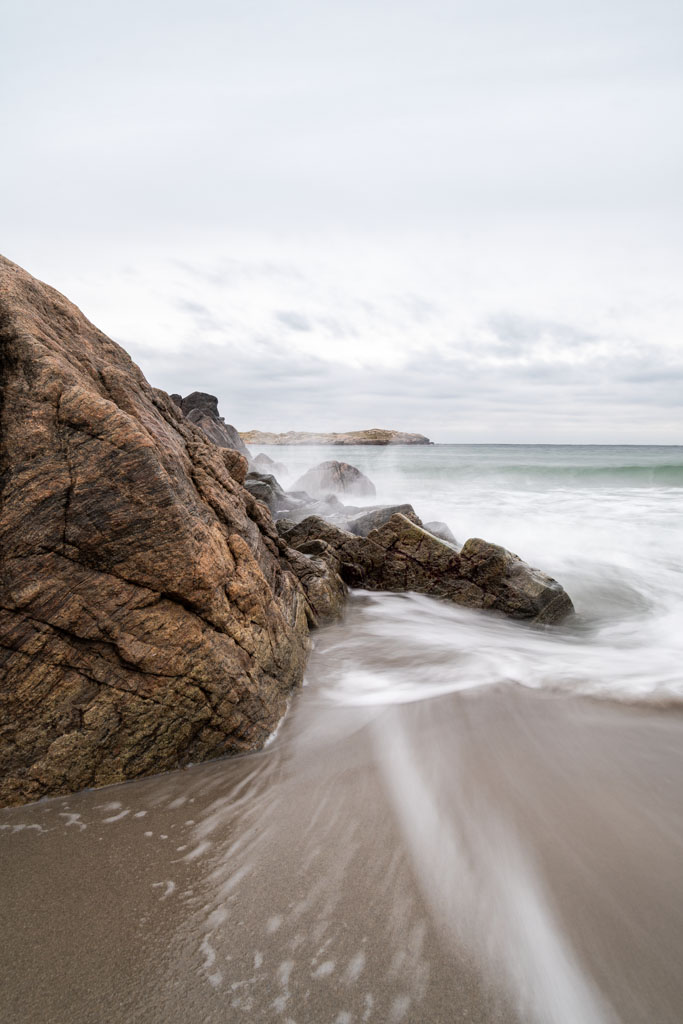 Bølger som treffer svaberg og smale sandflater ved Lista-strendene.