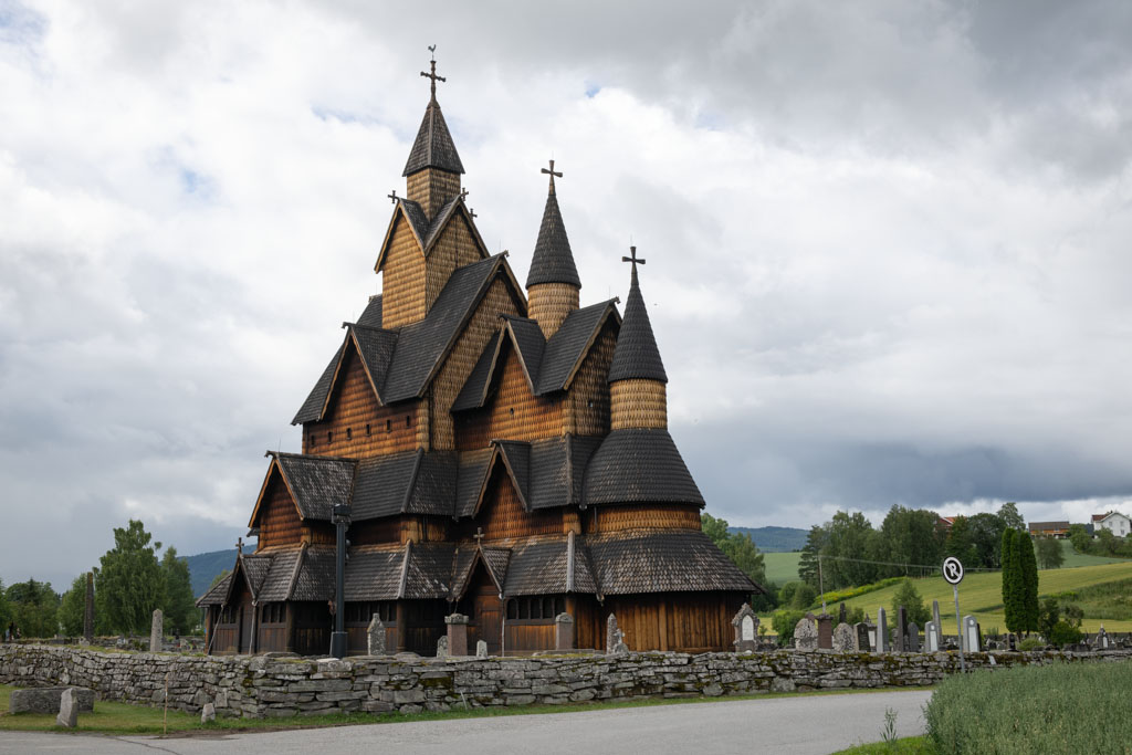 Heddal stavkirke i Telemark (2024), sett fra siden med gress og skyer i bakgrunnen.