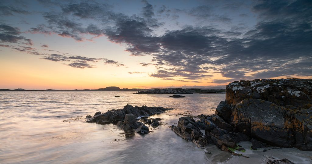 Solnedgang ved Einarsneset på Lista med svaberg i forgrunnen, rolig hav og dramatisk skydekke over horisonten.