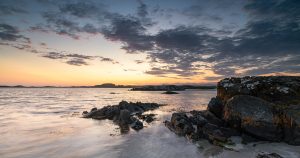 Solnedgang ved Einarsneset på Lista med svaberg i forgrunnen, rolig hav og dramatisk skydekke over horisonten.