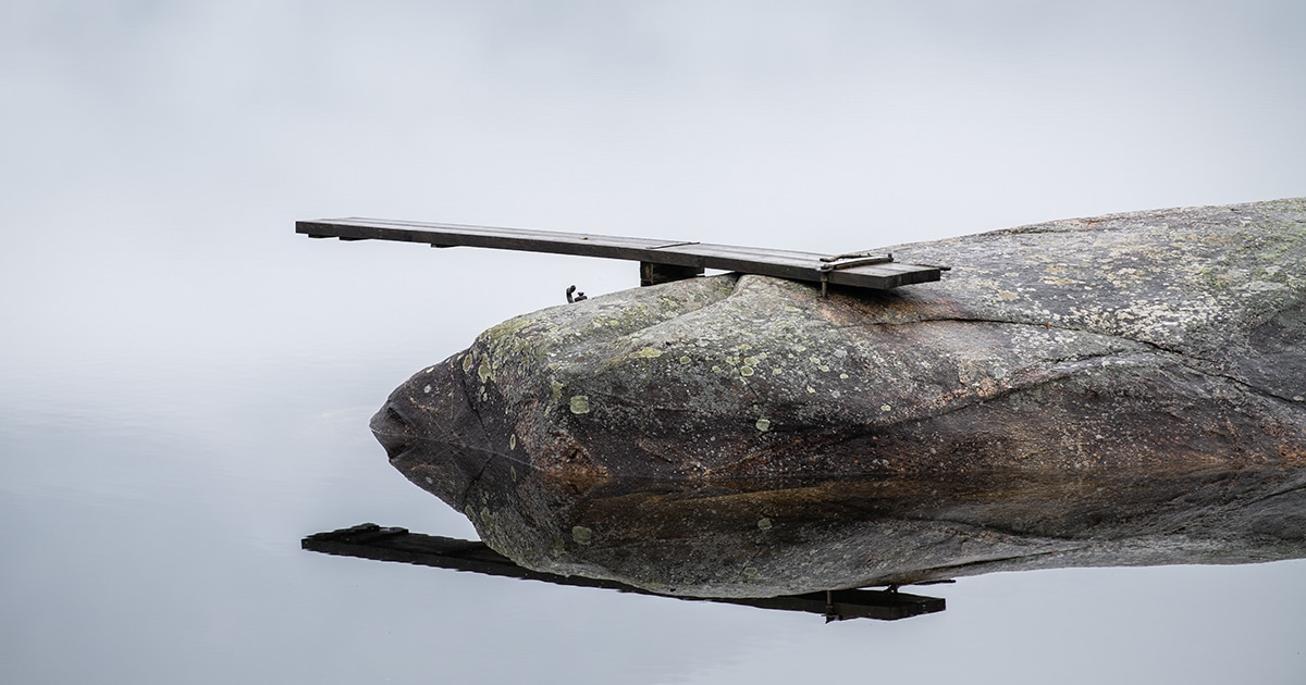 Stille vann og svaberg med liten brygge – minimalistisk kystmotiv.